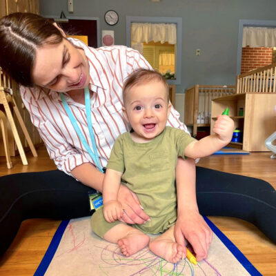 Teacher helping an infant draw with a crayon