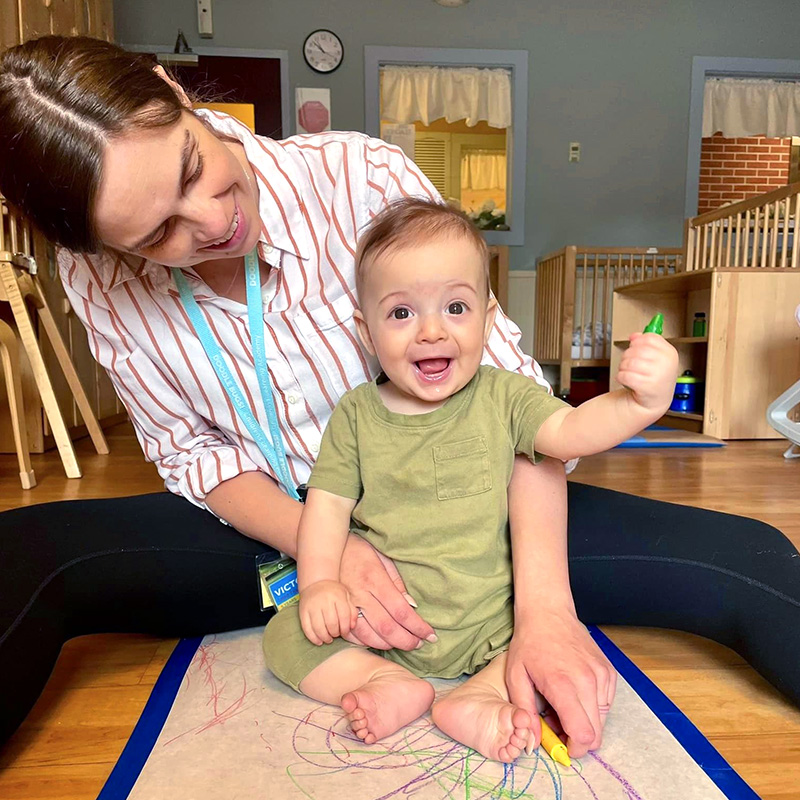 Teacher helping an infant draw with a crayon